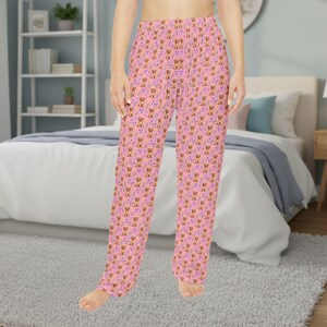 May include: Pink pajama pants with an all-over pattern of brown dogs, purple flowers, and yellow bones. The pants are made of a soft material and have a relaxed fit. The pajama pants are suitable for lounging or sleeping.