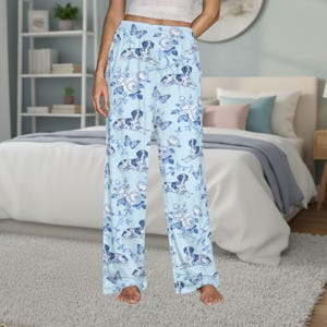 May include: Light blue pajama pants with a repeating pattern of dogs, butterflies, and floral elements. The pants have a wide-leg design and a comfortable, relaxed fit. The dog illustrations are in shades of blue and white.