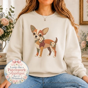 May include: A cream-coloured crewneck sweatshirt featuring a central graphic of a chihuahua dog designed with a multi-coloured patchwork pattern and small white flower accents. A circular badge on the lower left displays the text: Looks like a Patchwork Applique But it's Printed.