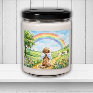Puede incluir: Un tarro de vela blanco con tapa negra. El tarro presenta una ilustración de acuarela de un perro con alas de ángel en un camino que conduce a un arcoíris. El nombre del perro, "Daisy", está en un letrero.