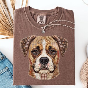 May include: A brown Comfort Colors t-shirt featuring a detailed patchwork design of a dog's face. The dog's face is made of various fabric patterns in shades of brown, beige, and white. A silver necklace with a pendant rests on the shirt.