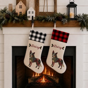 May include: Two off-white Christmas stockings featuring a colorful dog illustration, holly sprigs, and the name Daisy embroidered in red. One stocking has a black and white buffalo check cuff, while the other has a red and black buffalo check cuff.