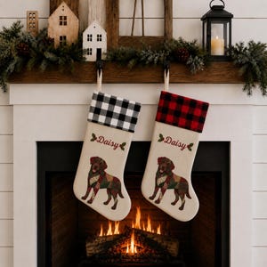 May include: Two cream-colored Christmas stockings featuring a brown dog illustration with a colorful patterned coat. One stocking has a black and white buffalo check cuff, the other a red and black check cuff. Both feature the name Daisy in red.
