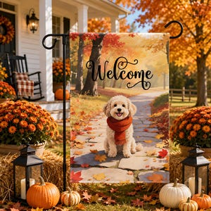 May include: A rectangular garden flag featuring a cream-colored dog wearing a red scarf, sitting on a stone path surrounded by fallen autumn leaves. The word Welcome is written in black cursive script above the dog against a fall forest background.