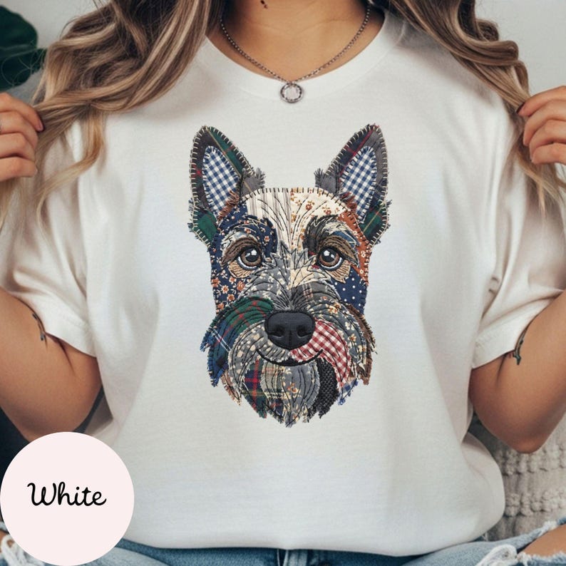 May include: White t-shirt featuring a patchwork design of a Scottish Terrier dog's face. The dog's face is composed of various fabric patterns, including plaid and floral prints. The t-shirt has a round neckline and short sleeves. The word "White" is printed on a white circle at the bottom.