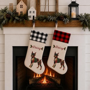 May include: Two off-white Christmas stockings featuring a Doberman dog illustration with a colorful patchwork pattern. One stocking has a black and white buffalo check cuff, the other a red and black check cuff. Both are embroidered with the name Daisy.