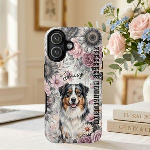 Può includere: Una custodia per telefono con il ritratto di un pastore australiano circondato da un motivo floreale di girasoli e rose nei toni del rosa, grigio e bianco. Il nome Daisy è stampato in corsivo e il testo AUSTRALIAN SHEPHERD è verticale.