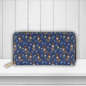 May include: A blue zippered wallet featuring a repeating pattern of brown and white dogs and colorful flowers. The wallet has a gold-colored zipper and a matching gold zipper pull. The background is a dark blue color.