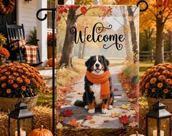 May include: A rectangular garden flag featuring a Bernese Mountain Dog wearing an orange scarf, sitting on a stone path covered in autumn leaves. The word Welcome is printed in black script at the top, set against a background of fall trees.