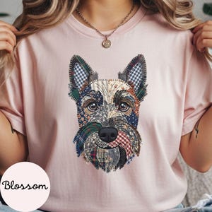 May include: A light pink t-shirt featuring a patchwork design of a dog's face. The dog's face is made up of various fabric patterns, including plaid and floral prints. The word "Blossom" is printed on the bottom left.