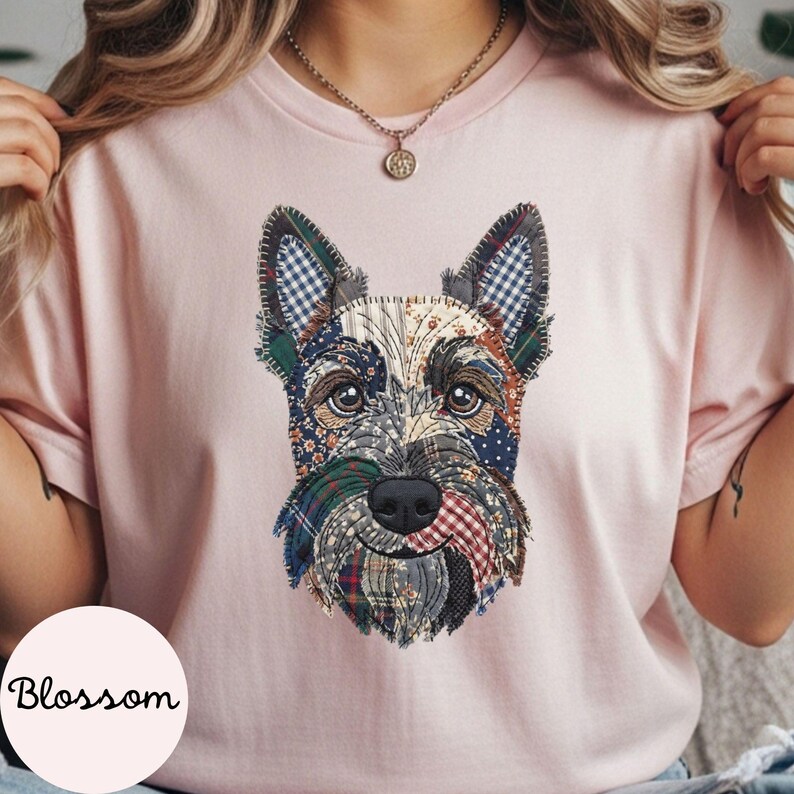 May include: A light pink t-shirt featuring a patchwork design of a dog's face. The dog's face is made up of various fabric patterns, including plaid and floral prints. The word "Blossom" is printed on the bottom left.