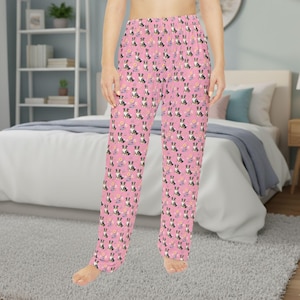 May include: Pink pajama pants with a repeating pattern of black, white, and brown dogs, along with small yellow and purple flowers. The pants are made of a soft material and have a relaxed fit.