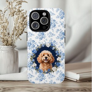 Könnte beinhalten: Weißes Handycase mit blauem Blumenmuster und einem Porträt eines Cocker Spaniels. Der Hund ist von einem blau-weißen Blumenkranz umgeben. Das Case hat ein schwarzes Kameramodul.