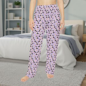 May include: Light purple pajama pants with a repeating pattern of black and white dogs and small yellow and purple flowers. The pants have a relaxed fit and a drawstring waist. The pajama pants are made of a soft, lightweight fabric.