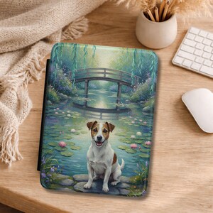 Può includere: Una custodia per tablet raffigurante una serena scena di stagno con un piccolo ponte di legno, salici piangenti e ninfee. Un Jack Russell Terrier è seduto sul bordo dello stagno. La custodia ha un bordo nero ed è su una superficie di legno.
