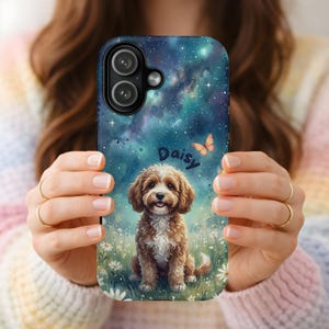 Könnte beinhalten: Eine Handyhülle mit einer Aquarellillustration eines braun-weißen Hundes namens Daisy, vor dem Hintergrund eines Sternenhimmels. Ein Schmetterling ist ebenfalls im Design enthalten. Die Hülle wird von einer Person gehalten.