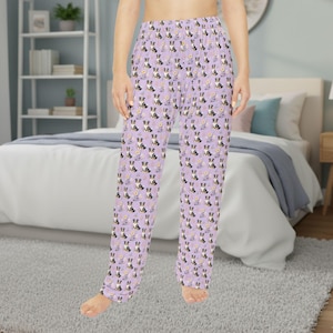 May include: Lavender pajama pants with a repeating pattern of black, white, and brown dogs, along with yellow flowers. The pants are made of a soft material and have a relaxed fit.