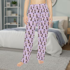 Könnte beinhalten: Helllila Pyjamahose mit einem sich wiederholenden Muster aus braunen Hunden, gelben Blumen und blauen Herzen. Die Hose ist aus einem weichen Material gefertigt und hat eine lockere Passform. Geeignet zum Entspannen oder Schlafen.