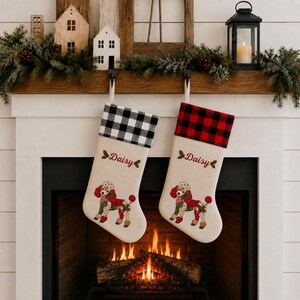May include: Two off-white Christmas stockings featuring a poodle graphic, the name Daisy in red script, and holly accents. One stocking has a black and white buffalo check cuff, while the other has a red and black buffalo check cuff.