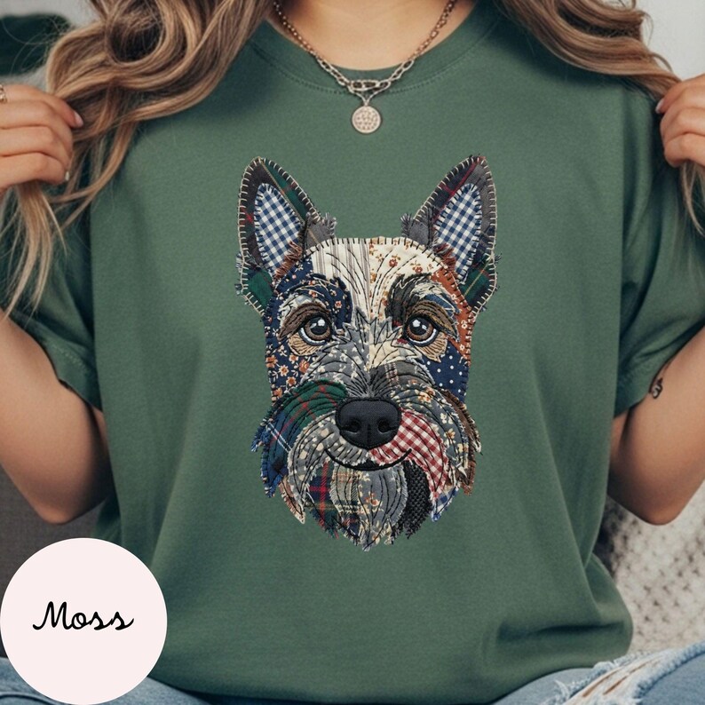 May include: A moss green t-shirt featuring a patchwork design of a Scottish Terrier dog. The dog's face is composed of various fabric patterns, including plaid and floral prints. The word "Moss" is printed on a white circle in the lower left corner.