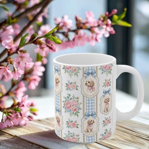 Puede incluir: Una taza de cerámica blanca con un patrón repetitivo de rayas verticales de cuadros vichy azul claro, ramos de flores rosas e ilustraciones de perros pequeños de color claro con lazos rosas, enmarcados en un borde decorativo con un lazo azul.