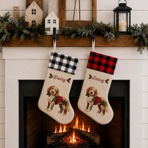 May include: Two cream-colored Christmas stockings featuring a goldendoodle dog illustration, holly accents, and the name Daisy printed in red. One stocking has a black and white buffalo check cuff, while the other has a red and black buffalo check cuff.