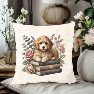 Op de afbeelding: Vierkant sierkussen met een lichtbruine puppy die op een stapel van drie boeken zit. Het kussen heeft een crèmekleurige achtergrond met bloemen en botanische illustraties in roze, bruin en groen.