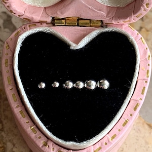 May include: A set of six silver ball earrings in a pink heart-shaped box with a gold clasp.