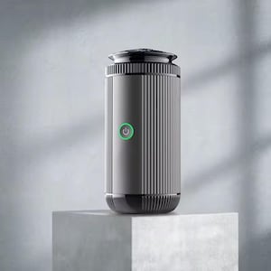 May include: A grey and black cylindrical air purifier with vertical ribbed detailing. It has a green power button and a modern design. The device is displayed on a white cube against a neutral background.
