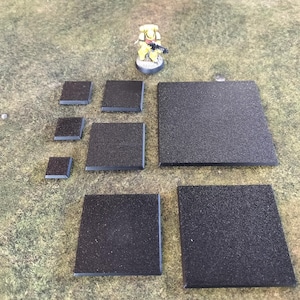 May include: A set of nine black square bases for miniature figures, ranging in size. The bases are made of a textured material and are ideal for tabletop gaming.