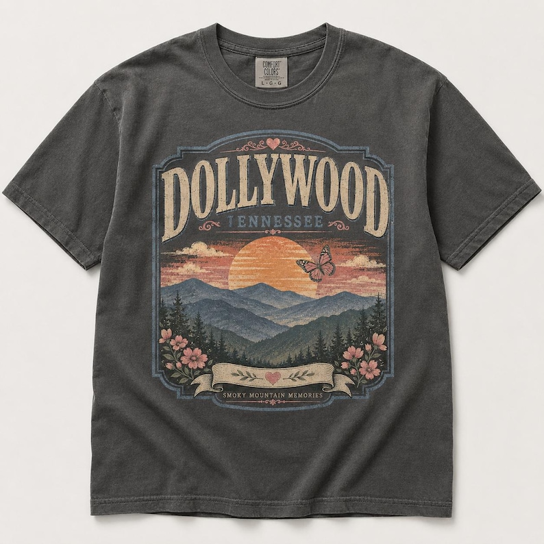 May include: A charcoal gray short-sleeve t-shirt featuring a graphic print of a sunset over mountains with the text DOLLYWOOD TENNESSEE and SMOKY MOUNTAIN MEMORIES. The design includes a butterfly, flowers, and hearts in muted orange, pink, and blue.