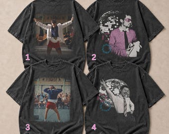 May include: Four charcoal gray short-sleeve t-shirts with graphic prints. Shirt 1 and 3 show a person in a white blazer or blue jacket with red shorts. Shirt 2 and 4 feature a person with a disco ball, pink glasses, and text accents.