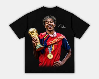 May include: A black short-sleeve t-shirt featuring a graphic print of a person holding a gold trophy. The person wears a red and blue jersey with the text "CAMPEDNES" and a gold medal. A white signature is visible above the person's shoulder.