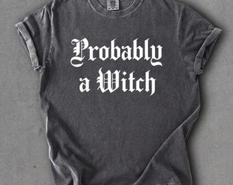 May include: A charcoal grey t-shirt with rolled sleeves featuring the white text 'Probably a Witch' in a gothic font. The shirt has a washed, vintage-style finish and a crew neckline. The word 'pepper' is printed in the top left corner.