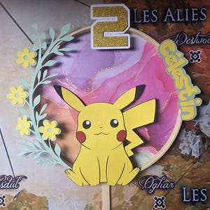 May include: A yellow Pikachu character cake topper with a green floral design and a gold number 2 on a pink and purple marbled background. The text "Celestin" is written in yellow on a green background.