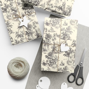May include: Three gift boxes wrapped in cream and black toile patterned paper with twine and white paper tags. The tags are shaped like a star, a heart, and a circle. A ball of twine and a pair of scissors are also in the image.