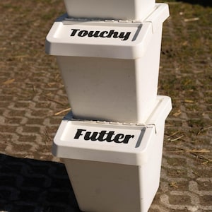 Könnte beinhalten: Drei weiße Plastikbehälter, die übereinander gestapelt sind. Der obere Behälter trägt die Aufschrift "Zusätze". Der mittlere Behälter trägt die Aufschrift "Touchy". Der untere Behälter trägt die Aufschrift "Futter".