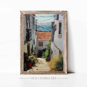 Pode incluir: Pintura emoldurada de uma rua estreita com edifícios brancos e telhados de telha vermelha. A obra de arte mostra uma cena costeira com vista para o mar. O texto "OLD CHARM ART" está na parte inferior da moldura. A moldura é dourada.