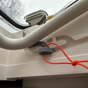 Op de afbeelding: Een wit dakluik met een grijze handgreep en een rood koord bevestigd aan een grijze stop. Het koord is in een knoop geknoopt.