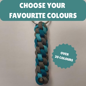 Può includere: Portachiavi intrecciato blu e grigio, con anello in metallo. Il testo "CHOOSE YOUR FAVOURITE COLOURS" è in alto e "OVER 20 COLOURS" in una forma a stella verde acqua.