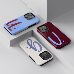 Könnte beinhalten: Drei Handyhüllen in verschiedenen Farben: Hellblau, Burgunderrot und Off-White. Jede Hülle hat ein einzigartiges Schriftzug-Design in kontrastierenden Farben. Die Hüllen werden auf einer weißen Oberfläche präsentiert.