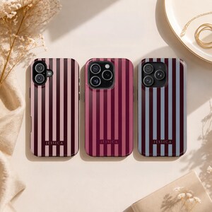Peut inclure: Trois coques de téléphone rectangulaires présentant des rayures verticales dans des combinaisons de couleurs variées : rose clair, bordeaux foncé, magenta et bleu ardoise. Chaque coque affiche le nom JESSICA en bas au centre.