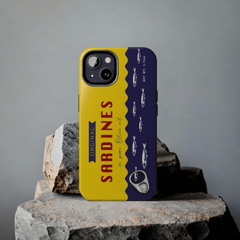 Phone case designed as a vintage sardine tin can with silver fish illustration and pull-tab detail on a bold yellow and navy background – retro foodie aesthetic.