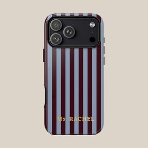 May include: A phone case with a vertical striped pattern in burgundy and light blue. The case has a black camera module with three lenses and the text "Ms RACHEL" in gold lettering.