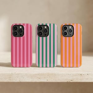 Könnte beinhalten: Drei Handyhüllen mit vertikalen Streifen. Die Hüllen zeigen rosa und rote, grüne und rosa sowie orange und rosa Streifen. Die Hüllen befinden sich auf einer hellen Oberfläche.