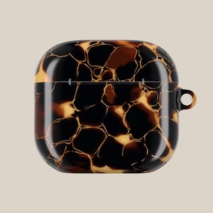 Może przedstawiać: Kwadratowe etui na AirPods z wzorem imitującym skorupę żółwia. Etui ma błyszczące wykończenie z mieszanką czarnych, brązowych i złotych odcieni. Posiada małą pętlę z boku do przymocowania do breloczka lub smyczy.