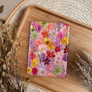 May include: A rectangular electronic reader cover featuring a vibrant, multi-colored floral pattern. The design displays a dense arrangement of painted flowers in shades of pink, yellow, orange, purple, red, and green, covering the entire surface.