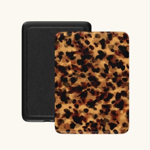 Op de afbeelding: Twee rechthoekige hoesjes, één zwart en één met een schildpadpatroon. Het schildpadontwerp heeft bruine en zwarte vlekken op een beige achtergrond. De zwarte hoes heeft een gestructureerd oppervlak. Waarschijnlijk voor een telefoon of tablet.