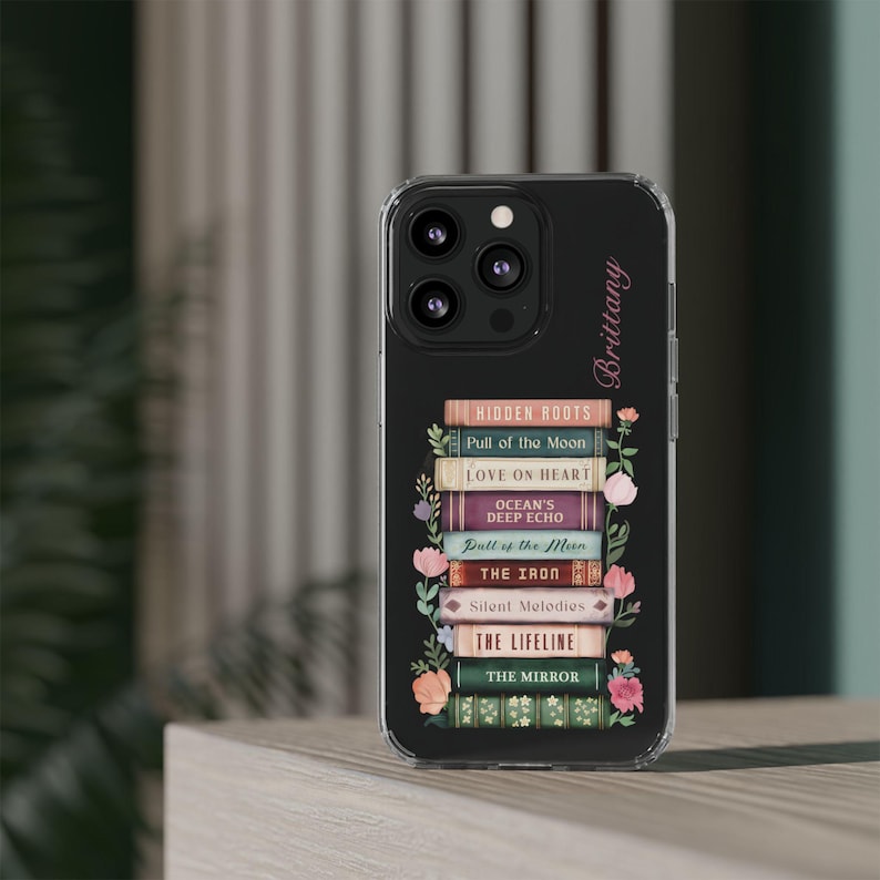 K&ouml;nnte beinhalten: Schwarze Handyh&uuml;lle mit einem Stapel B&uuml;cher, darunter Titel wie "Hidden Roots" und "Love on Heart", verziert mit floralen Elementen. Der Name "Brittany" ist in Schreibschrift geschrieben. F&uuml;r ein Smartphone.