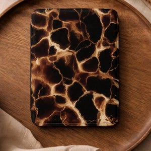 Op de afbeelding: Een rechthoekige hoes met een bruin en zwart giraffeprint patroon. De hoes is op een houten dienblad geplaatst. De hoes heeft een textuur en is waarschijnlijk ontworpen om een apparaat te beschermen.